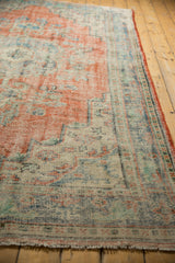 Heavily distressed Oushak rug corner with bare foundation, faded red and blue tones.