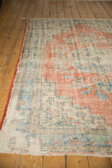 Distressed vintage Oushak rug corner showing bare foundation, fringed edge, and faded blue, red.