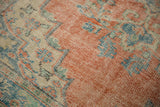 Distressed Oushak rug detail: faded cherry red, sky blue, and ivory floral motifs with pile wear.