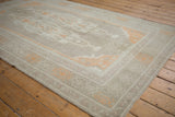 Distressed vintage Oushak rug corner showcasing low pile texture and pale tangerine vine border.