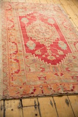 Distressed vintage Oushak rug with a faded raspberry red field, geometric medallion, and low pile texture.