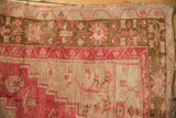 Textured close-up of vintage distressed Oushak rug corner, faded raspberry and bronze geometric motifs.