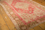 Secured edge of a vintage distressed Oushak rug, showing faded raspberry and bronze geometric patterns.