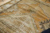 Distressed texture of a vintage Oushak rug's gold and ivory geometric pattern.