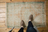 Distressed Oushak rug corner with fringed edge and leaf border in ivory, apricot, turquoise.