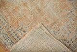 Distressed vintage Oushak rug close-up; low pile in apricot, ivory, navy tones, revealing woven back.