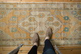 Distressed Oushak runner's saffron, silver, and aqua floral medallion, showing even wear.