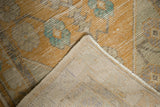 Distressed Oushak rug corner showing worn saffron yellow and aqua pile, revealing hand-knotted foundation.