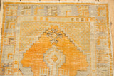 Distressed Oushak rug with prominent gold orange diamond medallion and ivory field.