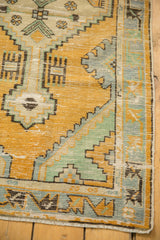 Decorative corner of a vintage Oushak rug, featuring distressed gold orange, mint, and blue geometric motifs.