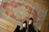 A person's view of a vintage distressed Oushak rug, showing its scale and faded red and ivory tones.
