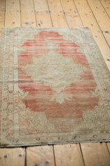Angled view of a distressed Oushak rug showing its soothing, faded striated red and ivory tones.