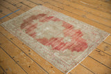 Angled view of a distressed Oushak rug showing its faded red and ivory Rococo-style pattern.