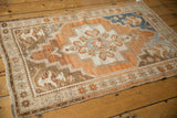 Distressed Oushak rug corner with copper floral starburst border, showing textured wear.