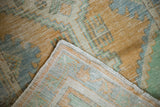 Distressed vintage Oushak rug corner, revealing faded gold, mint, blue pile, and secured edge.
