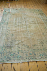 Oushak rug with distressed beige pile, worn leaf and rosette border, and fringe.