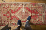 Distressed Oushak rug corner, showing faded cherry red geometric border and lattice motif.