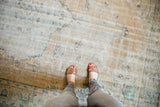 Distressed Oushak rug section with feet, highlighting faded ivory, beige, and sea-foam floral patterns.