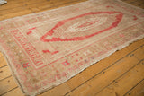 Distressed Oushak rug corner with faded bronze and pale raspberry red geometric border patterns.