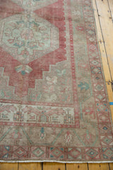 Distressed Oushak rug corner displaying geometric borders and muted floral motifs.