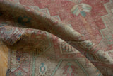 Folded distressed Oushak rug pile revealing faded rose, beige, and blue geometric patterns.