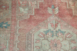 Close-up of distressed vintage Oushak rug, showing blush, beige, and blue geometric floral detail.