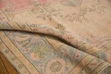 Detail of folded vintage Oushak carpet, with worn pile, scrolling vinery, and pastel hues.