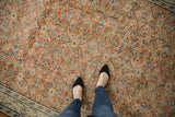 Feet on a hand-knotted vintage distressed Oushak rug, showing faded rust and ivory floral pattern.