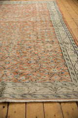 Distressed Oushak rug corner, with pale rust field, ivory border, exposed foundation, and fringe.