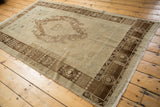 Corner of distressed Oushak rug with dark bronze germinating seed border, worn ivory pile.