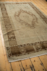 Distressed Oushak rug with ivory field, bronze medallion, and mostly even pile wear.