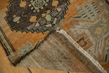 Folded distressed Oushak rug revealing low pile, hand knotted construction, and white fringe.