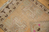 Distressed Oushak rug mat corner, with fringe, dark brown floral border, and worn texture.