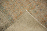 Distressed Oushak rug's muted orange and seafoam green pile with even wear, showing its foundation and fringe.