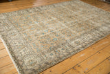 Angled view of a distressed vintage Oushak rug with faded beige and aqua floral vinery.