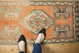 Stepped medallion and geometric motifs on a distressed vintage Oushak rug in orange, ivory, green.