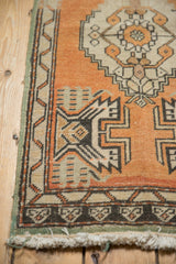 Distressed Oushak rug corner showing worn pile, orange rust field, and meandering vine border with fringe.