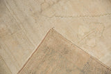 Close-up of a Distressed Oushak carpet corner, showing its low ivory pile and woven beige foundation.