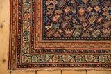 Antique Serbend rug corner with intricate terra cotta borders, navy floral motifs, and fringe.