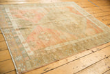 Fringed corner of distressed Oushak rug with blush, bronze, and blue geometric floral patterns.