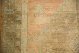 Distressed Oushak wool pile showing geometric floral motifs in blush, bronze, and powder blue.
