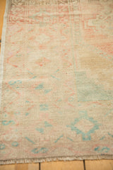 Distressed vintage Oushak rug close-up, showing faded rose and pale aqua patterns, worn pile, and fringe.