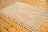 Side view of distressed Oushak rug showing intact selvage, muted blush and aqua tones.
