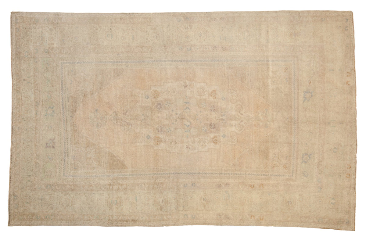 Distressed vintage Oushak carpet with a faint medallion and corner spandrels in soft ivory, sand, and pale blue.