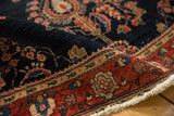Curled antique Mohajeran Sarouk rug edge, displaying deep navy floral field, wine red border, and fringe.