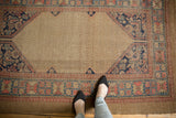 Feet on Antique Serab rug, highlighting beige lattice field and wide blush, navy borders.