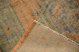 Distressed Oushak rug corner revealing apricot, blue, green pile, beige foundation, and fringe.