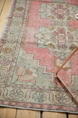 Distressed vintage Oushak rug showing blush, ivory, slate gray floral border detail with even wear.