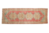 Distressed vintage Oushak runner with faded pink, red, slate blue-gray, and gold Rococo medallions.