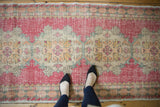 Faded red and sand distressed Oushak runner, showcasing floral motifs under feet.